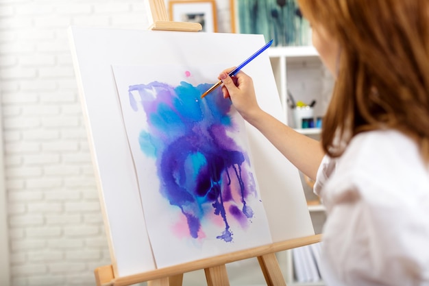 Young beautiful woman artist drawing abstract painting on an easel