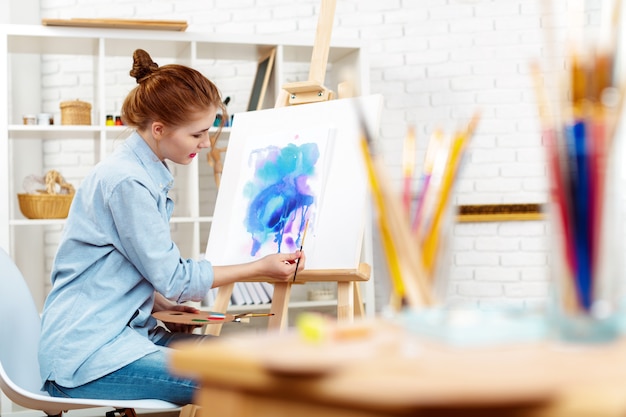 Young beautiful woman artist drawing abstract painting on an easel