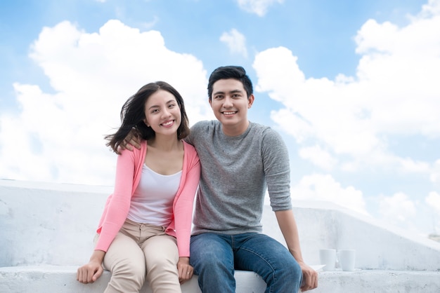 Young beautiful woman and asian man laugh against the dark blue sky with clouds