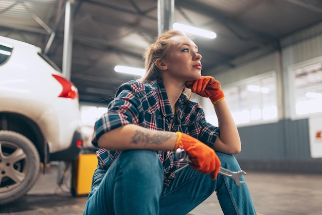 Young beautiful woman auto mechanic in casual comfortable cloth\
resting at auto service station