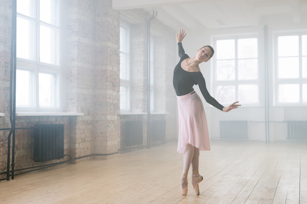 Young beautiful woman ballet dancer dressed in professional outfit pointe shoes and white tutu dancing in studio