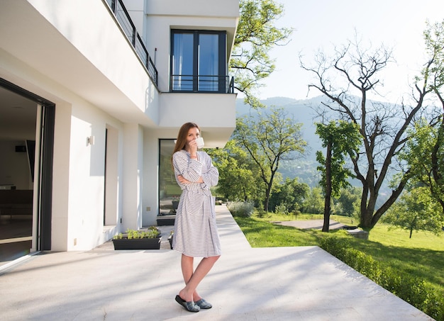 young beautiful woman in a bathrobe enjoying morning coffee in front of her luxury home villa