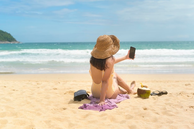 Молодая красивая женщина в бикини слушает музыку и пользуется смартфоном на пляже