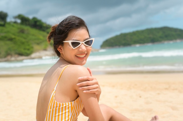 Giovane bella donna in bikini che ascolta musica e utilizza lo smartphone sulla spiaggia