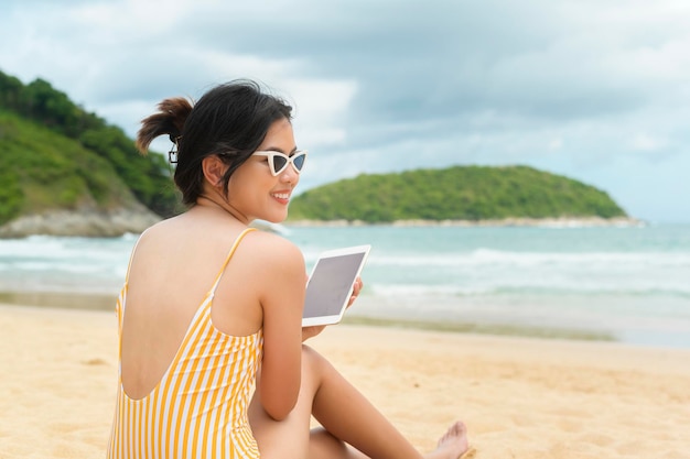 Giovane bella donna in bikini rilassante e utilizzando tablet sulla spiaggia