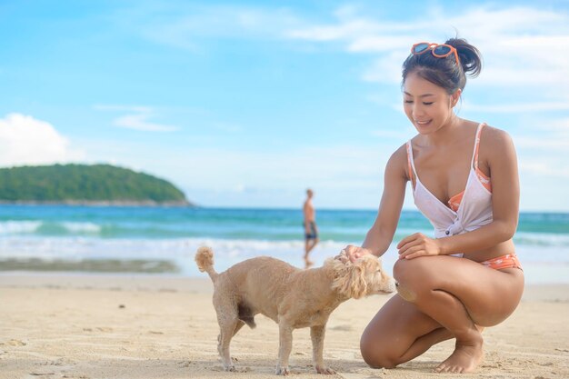 그녀의 강아지와 함께 비키니를 입고 해변에서 즐기고 휴식을 취하는 젊은 아름다운 여자