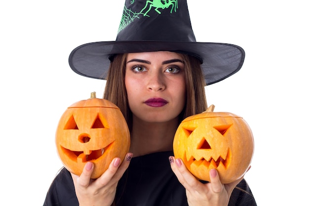 Young beautiful woman in black costume of witch holding two pumpkins on white background in studio