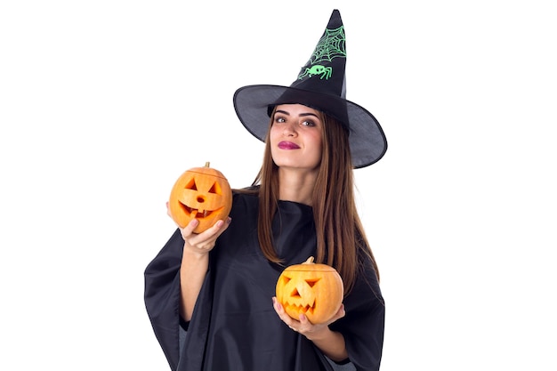 Young beautiful woman in black costume of witch holding two pumpkins on white background in studio