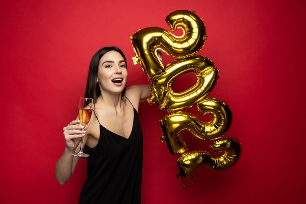 A young beautiful woman in a black dress holds the numbers 2022 and a glass of champagne