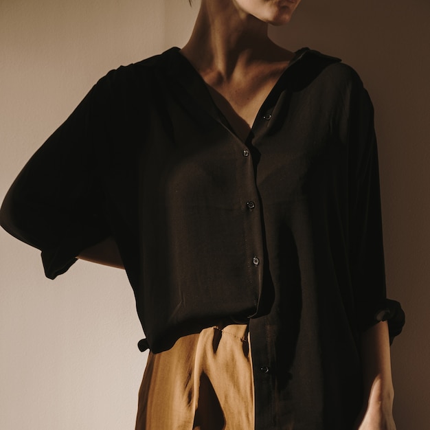 Young beautiful woman in black shirt and brown trousers staying against the wall