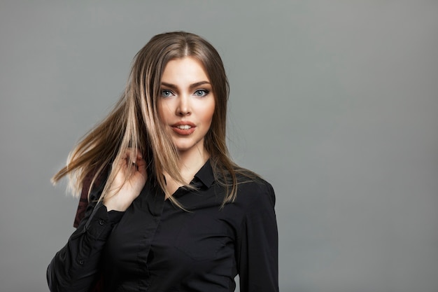 Young beautiful woman in a black shirt. Success and confidence,  Gray background. Space for text. Close-up.