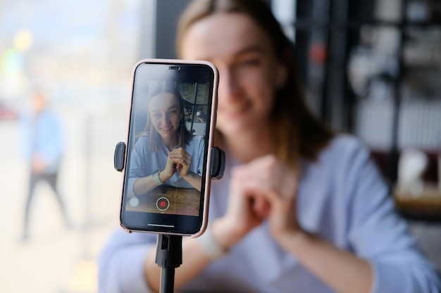 Foto una giovane e bella blogger che fa un video per il suo blog usando la telecamera di un telefono in un caffè