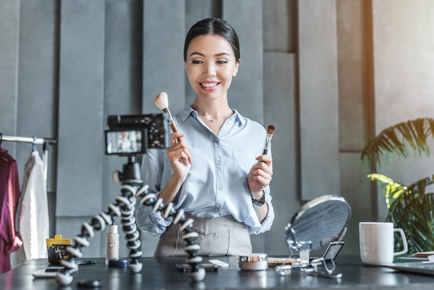 Young beautiful woman blogger using cosmetics while recording on digital camera