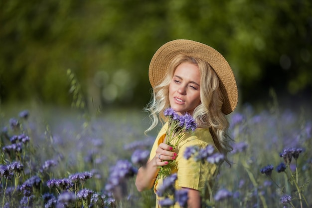 帽子をかぶった金髪の若い美しい女性は、紫色の花のフィールドを歩きます。夏。春。