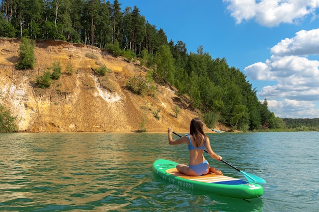 Giovane bella donna in bikini blu sta cavalcando a bordo di un sup dalle cave di dzerzhinsky.