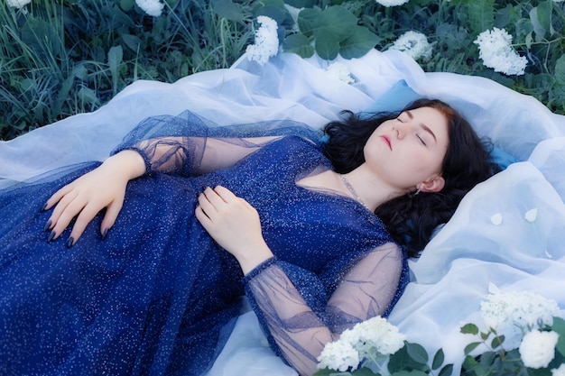 Молодая красивая женщина в голубом платье на траве с белыми цветами