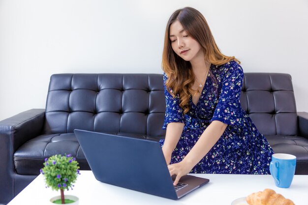 Young beautiful woman in blue dress working on her computer in her home living room