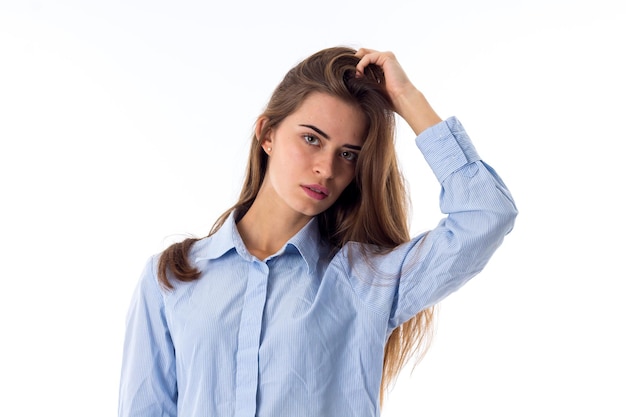 Young beautiful woman in blue shirt fixing her long hair on white background in studio