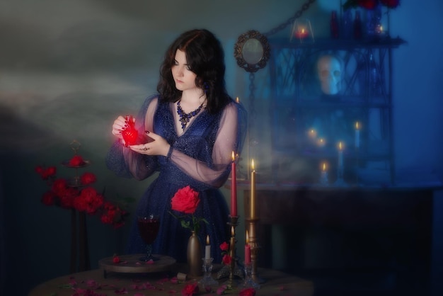 Young beautiful woman in blue vintage dress with red roses makind potion in dark room