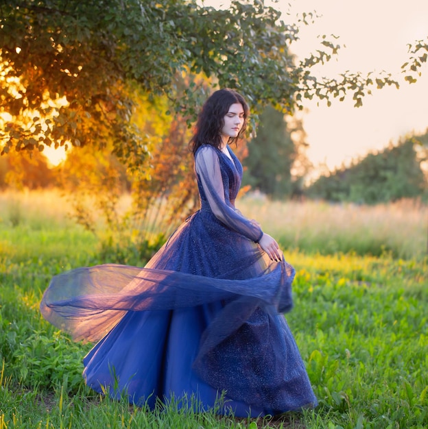 Young beautiful woman in blue vintage dress with white flowers at sunset