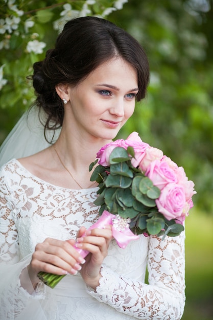 Young beautiful woman, bride with wedding bouquet in blooming garden