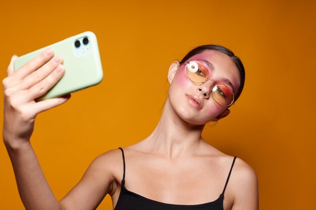 Young beautiful woman bright makeup posing black jersey with a phone in hand yellow background unalt.