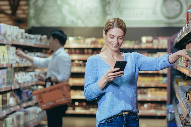 Young beautiful woman buyer in a supermarket chooses goods in the store housewife looks at the phone