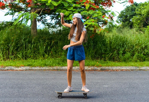 스케이트보드를 타고 웃는 모자를 입은 아름다운 젊은 여성