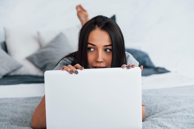 young beautiful woman in casual clothes lying down at home alone with laptop.
