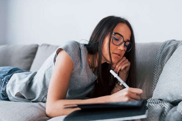 Foto giovane bella donna in abiti casual sdraiato a casa da solo con blocco note e penna.