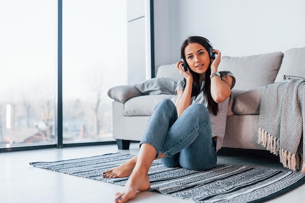 Young beautiful woman in casual clothes sitting at home alone and listening to the music in headphones.