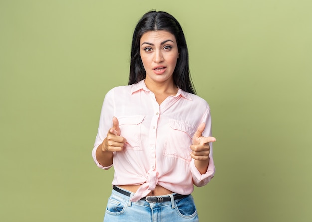 Young beautiful woman in casual clothes smiling confident pointing with index finger  standing over green wall