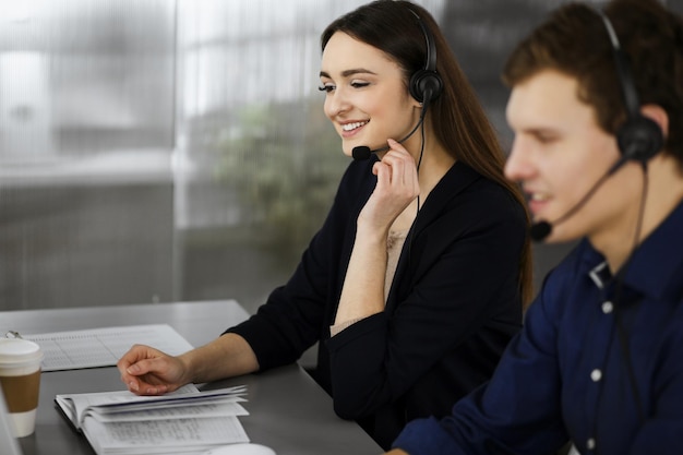 Photo young beautiful woman casual dressed in headsets is listening to a company's client, while she is sitting at the desk, working together with a male colleague in a modern office. focus on woman. call c