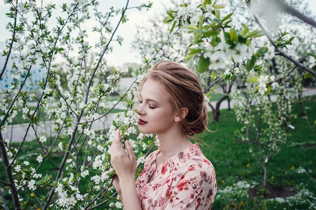 Young beautiful woman in the cherryblossoming garden A woman face is hidden by white flowers and cherry branches Spring nature Sweet aroma Blooming spring cherry tree Sweet fragrant smell