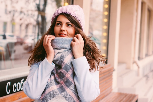 Young beautiful woman in coat and hat in late autumn or early winter on city street enjoying life