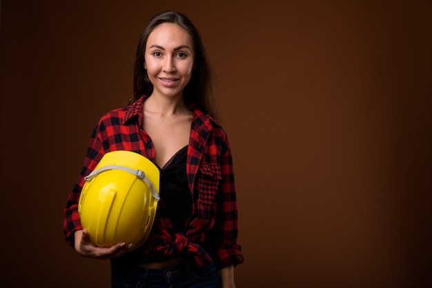 Young beautiful woman construction worker against brown background