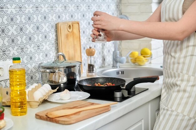 Young beautiful woman cooking at home in kitchen, fries eggs with sausages mushrooms and paprika in frying pan. Homemade fresh healthy food, hobbies and leisure