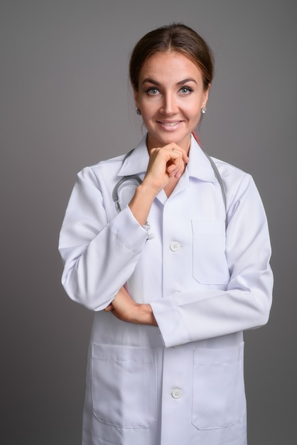 Young beautiful woman doctor against gray wall