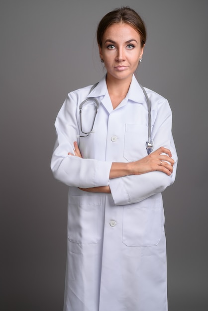 Young beautiful woman doctor against gray wall