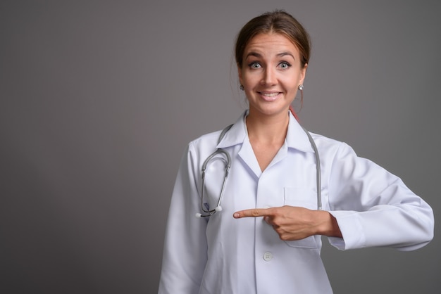 Young beautiful woman doctor against gray wall