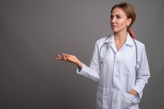 Young beautiful woman doctor against gray wall