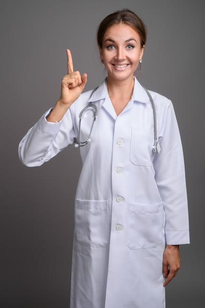 Young beautiful woman doctor against gray wall