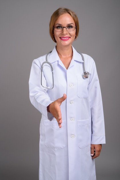 Young beautiful woman doctor with blond hair against gray backgr