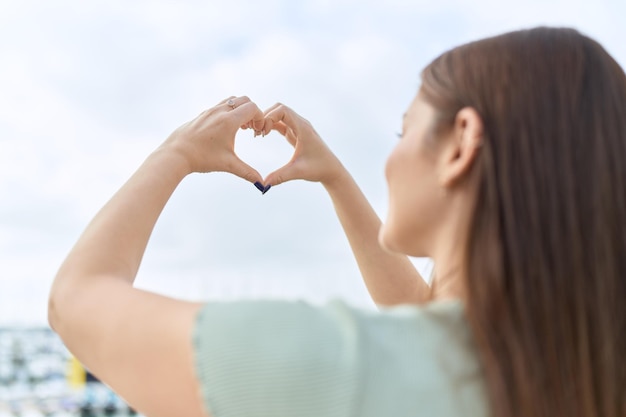 海辺で手でハートのジェスチャーをしている若い美しい女性