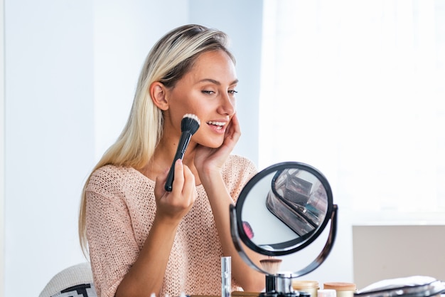 Young beautiful woman doing her make up near mirror