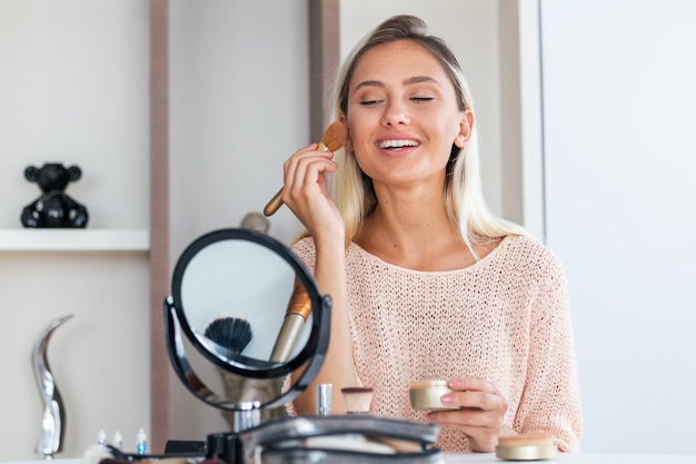 Photo young beautiful woman doing her make up near mirror
