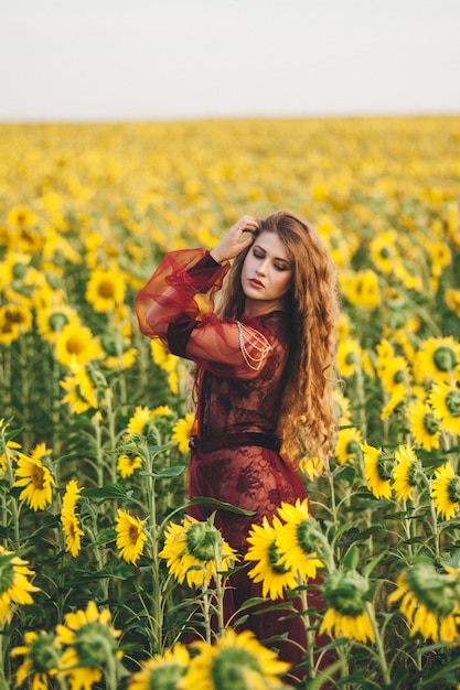 Young beautiful woman in a dress among blooming sunflowers. Agro-culture. 