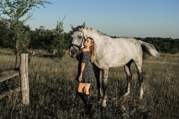 young beautiful woman in dress standing near white horse in a field in the summer rustic countryside