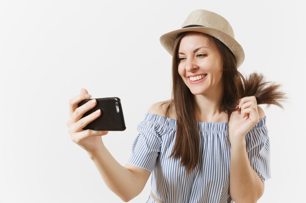 Giovane bella donna vestita vestito blu, cappello facendo selfie girato sul telefono cellulare o videochiamata isolato su sfondo bianco. persone, emozioni sincere, concetto di stile di vita. zona pubblicità. copia spazio.