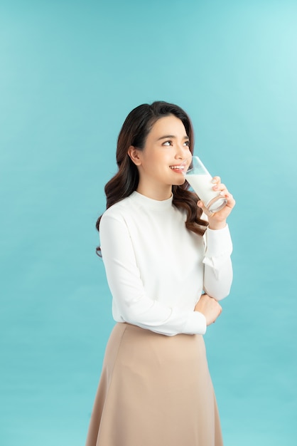 Young beautiful woman drink a glass of milk on blue background